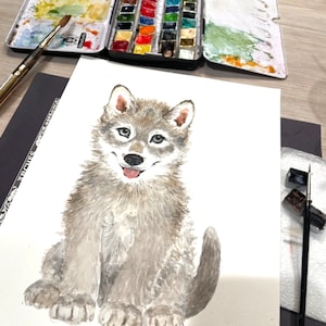 May include: Watercolor painting of a gray wolf pup sitting on a white background. The wolf pup has a light gray coat with darker gray markings. It has a pink nose and tongue, and its eyes are brown. The painting is done in a realistic style.