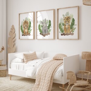May include: Three framed watercolor illustrations of baby animals in a jungle setting. The illustrations feature a lion, a rhinoceros, and a cheetah. Each illustration is framed in a light brown wood frame and set against a white wall.
