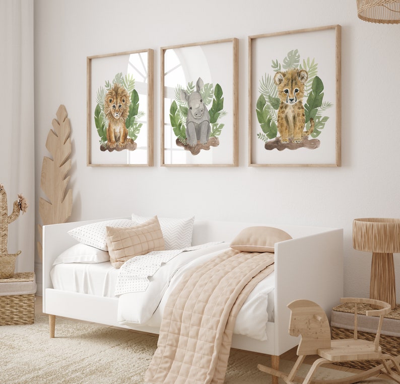 May include: Three framed watercolor illustrations of baby animals in a jungle setting. The illustrations feature a lion, a rhinoceros, and a cheetah. Each illustration is framed in a light brown wood frame and set against a white wall.