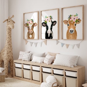 Puede incluir: Tres impresiones enmarcadas de pinturas de acuarela de vacas con coronas de flores. Las vacas son marrones, negras y blancas, y marrones. Las impresiones est&aacute;n colgadas en una pared blanca sobre un banco de madera con contenedores de almacenamiento.