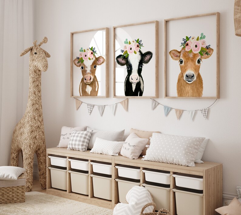 Puede incluir: Tres impresiones enmarcadas de pinturas de acuarela de vacas con coronas de flores. Las vacas son marrones, negras y blancas, y marrones. Las impresiones est&aacute;n colgadas en una pared blanca sobre un banco de madera con contenedores de almacenamiento.