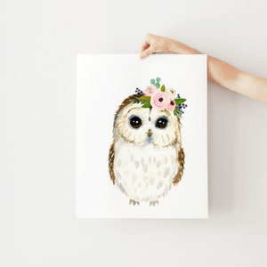 May include: A watercolor painting of an owl wearing a pink and white flower crown. The owl has brown and white feathers and large, dark eyes.