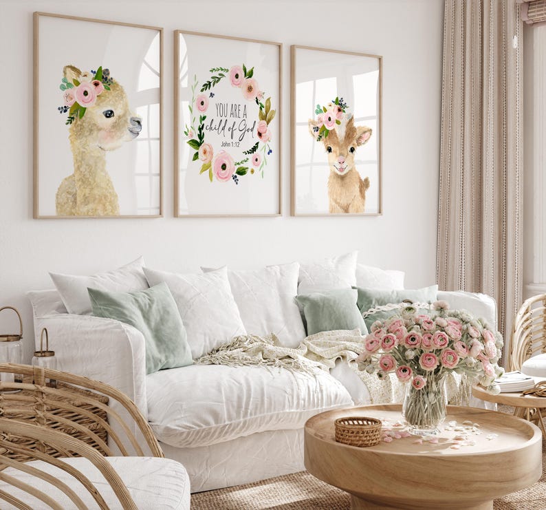 Pu&ograve; includere: Tre stampe ad acquerello raffiguranti un lama, una capra e una ghirlanda di fiori con il testo "You are a child of God, John 1:12". Le stampe sono incorniciate e appese a un muro bianco sopra un divano bianco con un'arrangiamento floreale su un tavolino da caff&egrave; in legno.