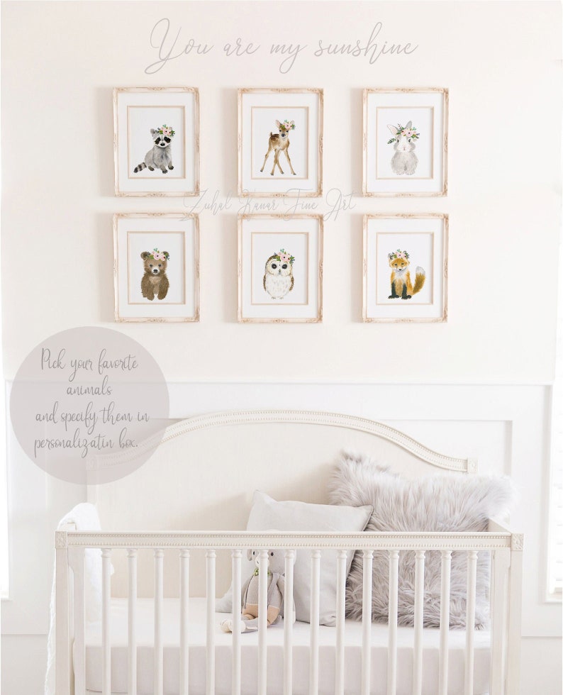 May include: Six framed watercolor illustrations of woodland animals with floral crowns, including a raccoon, deer, rabbit, bear, owl, and fox. The frames are white with a distressed finish and are hung on a white wall. The text "You are my sunshine" is written above the frames. The text "Pick your favorite animals and specify them in personalization box." is written below the frames.
