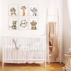 May include: A set of six watercolor animal prints featuring a monkey, giraffe, elephant, zebra, cheetah, and a floral wreath with the name "Carla" in the center. The prints are displayed on a white wall above a white crib with a white ruffle skirt.