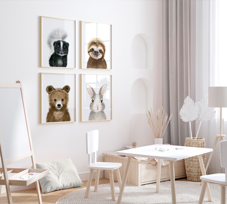 Op de afbeelding: Vier ingelijste dierillustraties in een witte kamer. De illustraties tonen een beer, een konijn, een luiaard en een stinkdier. De illustraties hangen aan een witte muur boven een witte tafel en stoelen.