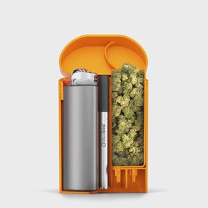 May include: An orange, rectangular container with a hinged lid, holding a silver lighter, a black and silver pen with "MicroGrind" printed on it, and a pile of green buds. The container is open, revealing its contents.