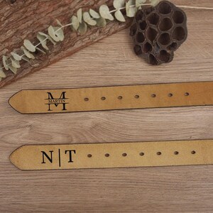 May include: Two tan leather belts with personalized initials and names. One belt is stamped with "MARTIN" and the initials "M" and "I". The other belt is stamped with the initials "N" and "T". Both belts have several holes for adjustment.