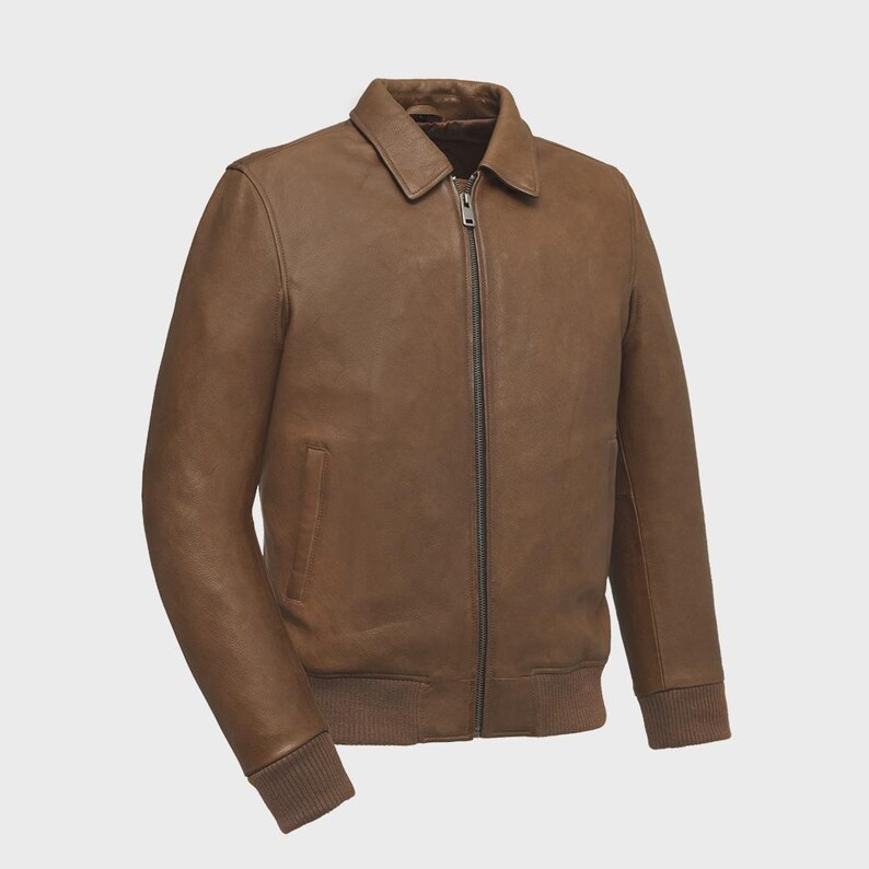 May include: A brown leather jacket with a collared neckline and a full-length zipper. The jacket features a ribbed knit hem and cuffs, and a small pocket on the left side. The jacket is a medium brown color.