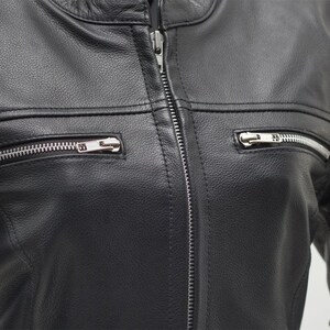 May include: Close-up of a black leather jacket with a silver zipper closure and two zippered pockets. The jacket has a classic design with a round collar and horizontal seams across the chest.