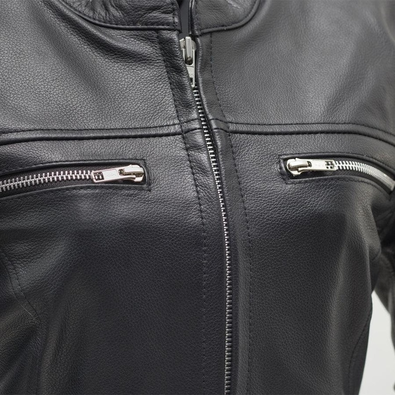 May include: Close-up of a black leather jacket with a silver zipper closure and two zippered pockets. The jacket has a classic design with a round collar and horizontal seams across the chest.