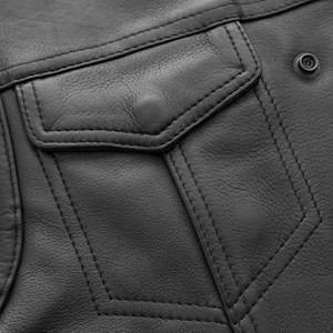 May include: Close-up of a black leather jacket detail. The image shows a pocket with a button closure, decorative stitching, and a snap closure. The leather has a textured appearance.