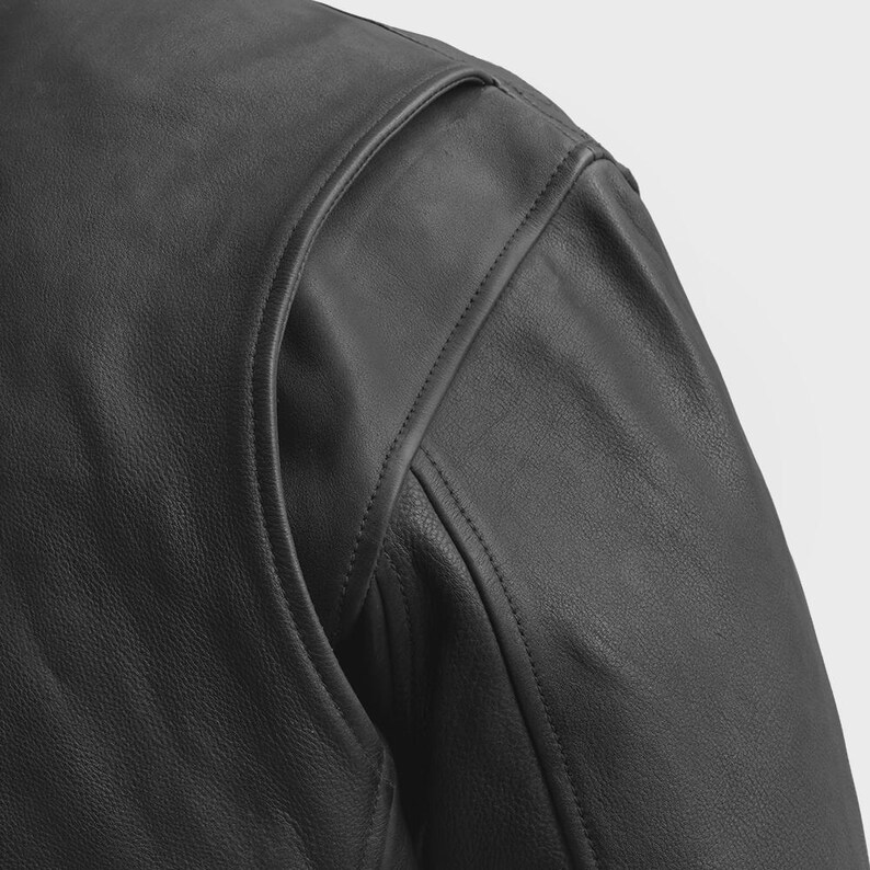 May include: Close-up of a black leather jacket shoulder. The jacket features a padded shoulder design with visible stitching details. The leather has a smooth, matte finish.