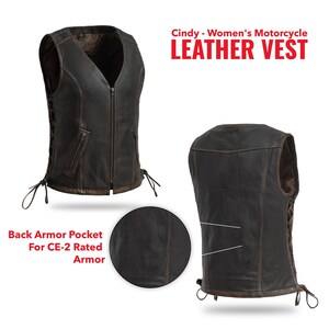 Pu&ograve; includere: Un gilet da moto in pelle marrone con zip frontale, lacci laterali e tasche. Il gilet ha uno scollo a V e una tasca posteriore per l'armatura. Il testo "Cindy - Women's Motorcycle LEATHER VEST" &egrave; visualizzato in rosso.