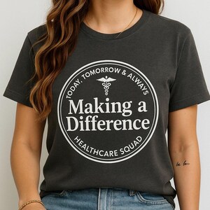 Peut inclure: Un t-shirt gris foncé avec un graphique circulaire blanc qui dit "Today, Tomorrow & Always Making a Difference Healthcare Squad". Le graphique comprend également un symbole de caducée.