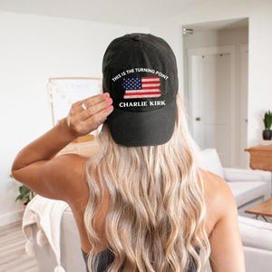 May include: Black baseball cap with the text "THIS IS THE TURNING POINT" and "CHARLIE KIRK" printed on the front. The cap features a distressed American flag design in red, white, and blue.