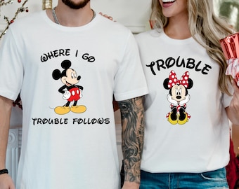 Könnte beinhalten: Weiße T-Shirts mit passenden Cartoon-Grafiken. Ein Shirt zeigt Micky Maus mit dem Text "Where I Go Trouble Follows". Das andere Shirt hat Minnie Maus mit dem Wort "Trouble".