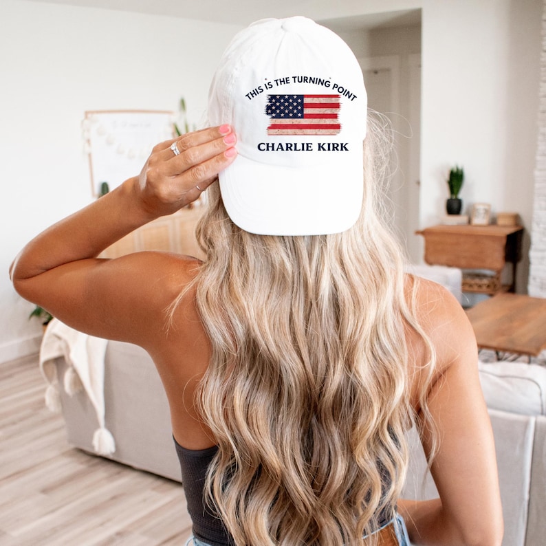 May include: White baseball cap with the text "THIS IS THE TURNING POINT" above a distressed American flag graphic and the name "CHARLIE KIRK" below. The cap is a classic six-panel design.