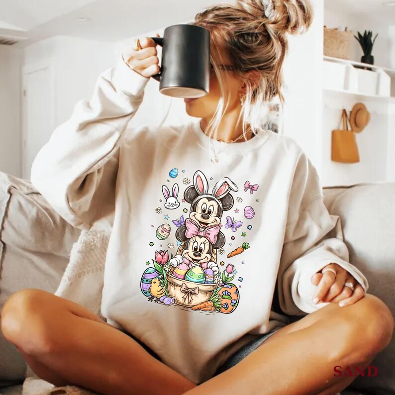 K&ouml;nnte beinhalten: Cremefarbenes Sweatshirt mit einem farbenfrohen Oster-Motiv von Mickey und Minnie Mouse mit Hasenohren. Das Design umfasst Ostereier, Schmetterlinge, Karotten und einen Korb. Das Sweatshirt hat eine lockere Passform.