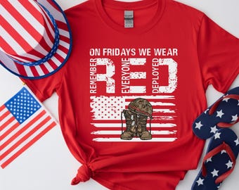 May include: A red t-shirt with the text "On Fridays We Wear Red" and an American flag design. The design includes military boots, a helmet, and dog tags. Additional patriotic items include a red, white, and blue hat, a small American flag, and star-spangled flip-flops.