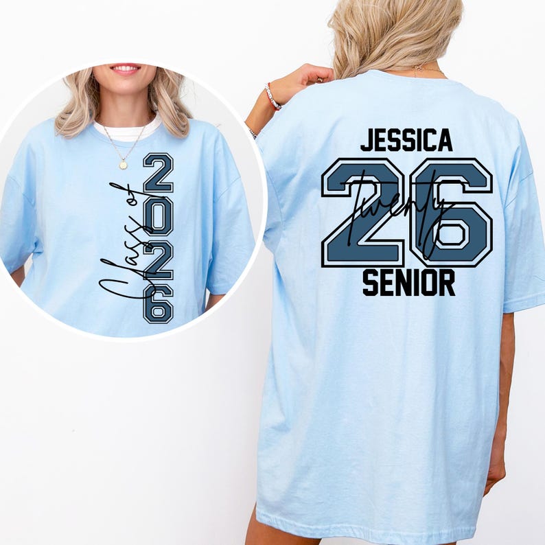 Puede incluir: Camiseta azul claro con "Class of 2026" impreso verticalmente en la parte delantera. La parte trasera de la camiseta muestra el nombre "Jessica", el n&uacute;mero "26" y la palabra "SENIOR" en una fuente de estilo universitario. Corte holgado.
