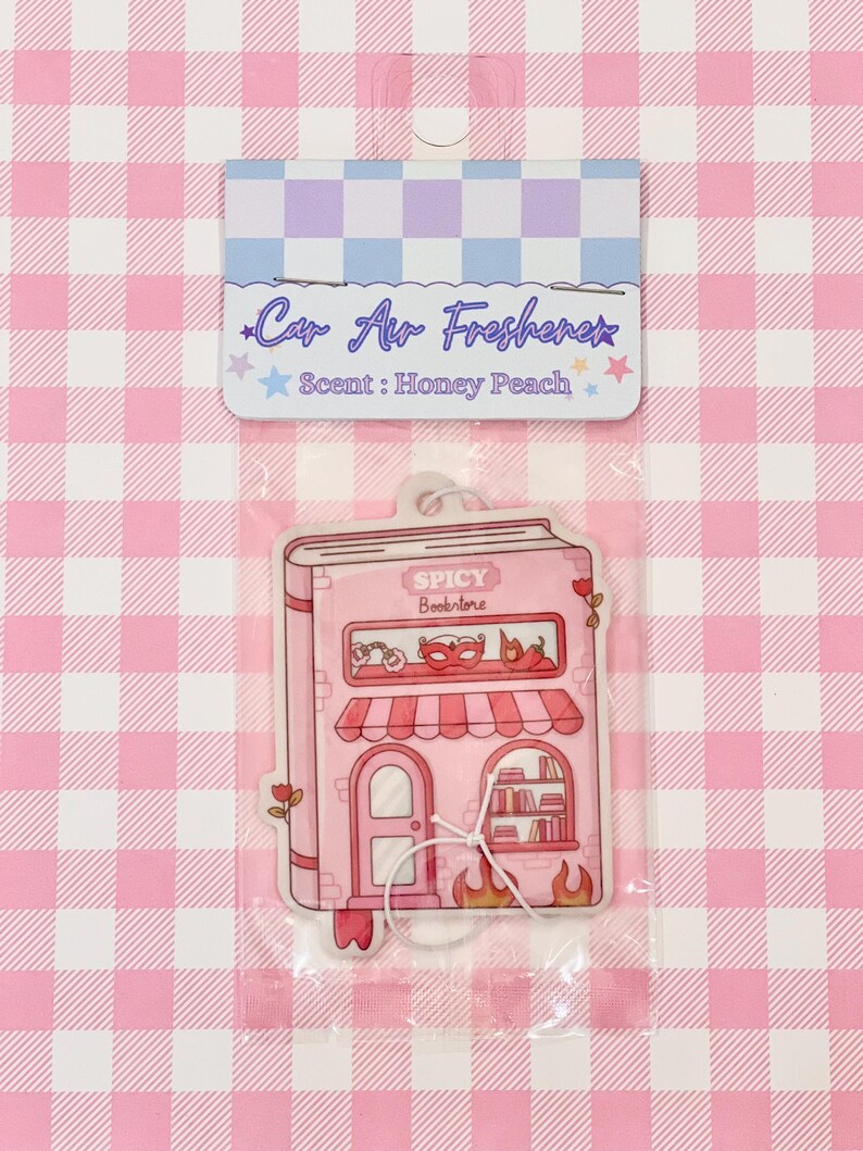 May include: A pink car air freshener shaped like a book, with the text "Spicy Bookstore." The top of the packaging reads "Car Air Freshener" and "Scent: Honey Peach."