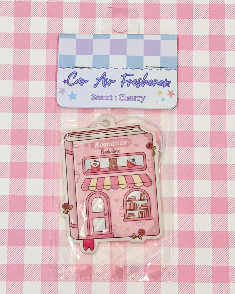 May include: Pink car air freshener in a clear plastic package. The air freshener is shaped like a pink bookstore with the words "Romance Bookstore" on the front. The packaging reads "Car Air Freshener" and "Scent: Cherry".