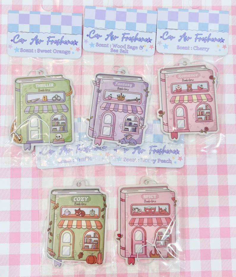 May include: Air fresheners in the shape of illustrated book storefronts. Each has a different theme: Thriller, Fantasy, Romance, Cozy, and Spicy. The packaging reads "Car Air Freshener" and lists scents like Sweet Orange and Cherry.