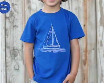 Peut inclure: Un t-shirt bleu roi avec un dessin au trait blanc d'un voilier. Le t-shirt à manches courtes semble être fait d'une matière douce. Le texte "True Royal" est dans un cercle bleu en haut à gauche. Pour enfant.