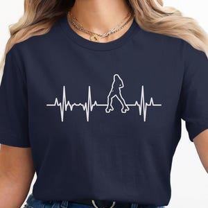 May include: Navy blue t-shirt featuring a white graphic of a roller skater within a heartbeat line. The design is simple and clean, perfect for roller skating enthusiasts. The shirt is made of a soft material.