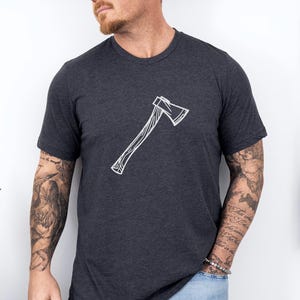 May include: Dark gray heather t-shirt featuring a white axe graphic. The axe design is centered on the chest. The shirt has a crew neck and short sleeves. The words "Dark Grey Heather" are in a circular design in the upper left corner.