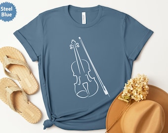 May include: Steel blue t-shirt featuring a white outline of a violin and bow. The shirt is styled with a pair of beige sandals, a brown hat, and a small bouquet of dried flowers. The shirt is made of a soft material.