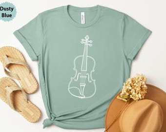 May include: A dusty blue t-shirt featuring a white outline of a violin. The shirt is paired with woven sandals and a tan hat with a dried flower. The shirt is a light, muted color, and the violin design is simple and elegant.