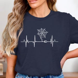 May include: Navy blue t-shirt featuring a white graphic of a spider web connected to a computer mouse, integrated into a heartbeat line design. The word "Navy" is in a navy blue circle in the upper left corner.
