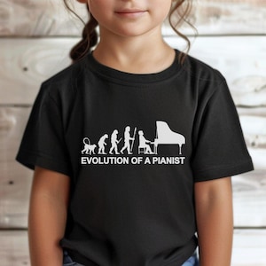 May include: Black t-shirt featuring a white graphic of the evolution of a pianist. The design shows a progression from a primate to a person playing a grand piano. The text "EVOLUTION OF A PIANIST" is below the graphic.