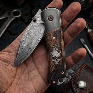 May include: A folding pocket knife featuring a Damascus steel blade with a wavy pattern. The handle is crafted from dark wood with an engraved flaming skull design, accented by copper-colored rivets and a metallic bolster near the pivot point.