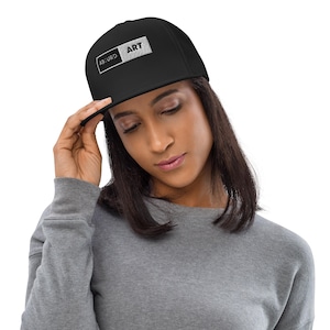 Puede incluir: Gorra negra de ala plana con las palabras "ABSURD ART" bordadas en un parche rectangular. La gorra la lleva una persona que viste una sudadera gris.