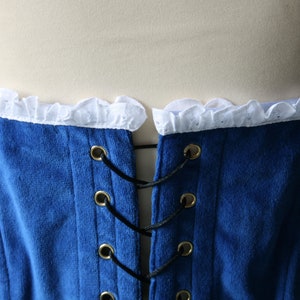 May include: Blue velvet corset with white lace trim and black lacing. The corset has gold metal eyelets and is tied at the back.