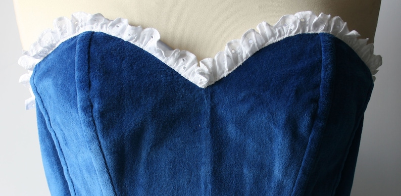 May include: A strapless blue velvet bodice with a white lace trim around the neckline.