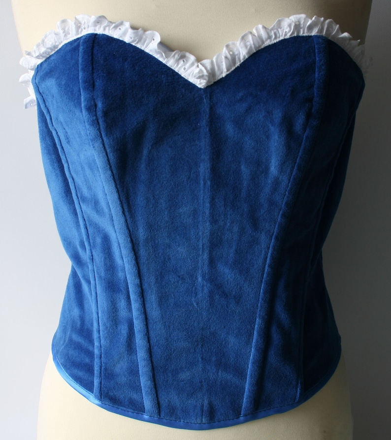 May include: A blue velvet corset with white lace trim. The corset has a sweetheart neckline and boning along the front.