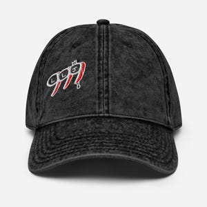Puede incluir: Gorra de béisbol negra de aspecto desgastado con visera curva. La gorra presenta el texto bordado "999" en blanco con detalles rojos y una pequeña corona. Tiene un diseño clásico de seis paneles y una correa ajustable.