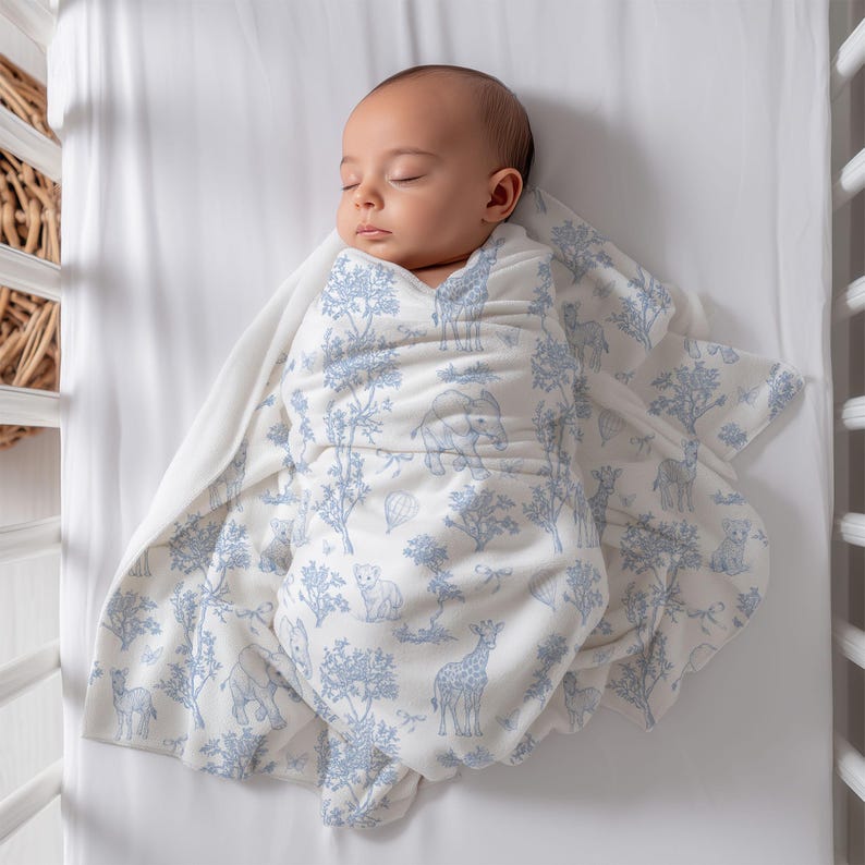 May include: A sleeping baby wrapped in a white and blue patterned swaddle blanket. The blanket features a repeating design of trees, giraffes, elephants, and other animals. The baby is lying in a white crib.