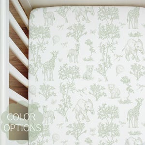 May include: A white fitted crib sheet with a repeating pattern of safari animals and trees in a soft green color. The design includes elephants, giraffes, zebras, and lions. The words "COLOR OPTIONS" are visible in the lower left corner.