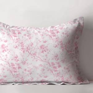 Peut inclure: Une taie d'oreiller blanche avec un motif floral rose. Le motif présente de délicates fleurs et branches roses sur un fond blanc. La taie d'oreiller a un bord volanté.