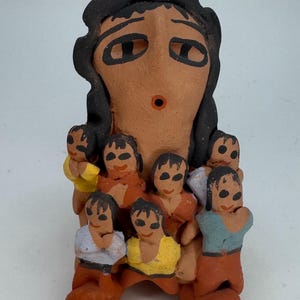 May include: A handcrafted ceramic figurine depicting a woman surrounded by several small figures. The woman has dark hair and a brown complexion. The smaller figures wear various colored clothing, including yellow, orange, and blue. The figurine is likely a decorative item.
