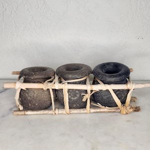 May include: Three dark gray, textured ceramic pots with wide openings, secured to a wooden frame with natural twine. The pots are arranged side-by-side, suggesting a decorative or functional display piece.