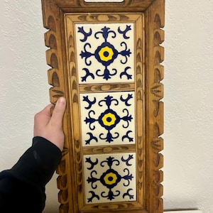 May include: Rectangular wooden serving tray with three decorative ceramic tiles. The tiles feature a white background with a blue and yellow floral pattern. The tray has carved details and integrated handles.