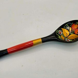 May include: A wooden spoon with a black handle and bowl, featuring a red and gold painted handle. The bowl is decorated with orange berries, yellow leaves, and white flowers. A traditional folk art item.