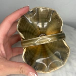 May include: A small, ceramic basket with a handle. The basket has a ruffled edge and a glossy, brown and gold finish. The handle is a matching brown color. The basket is held by a person.