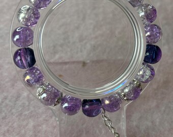 May include: A purple and silver bracelet with a dragonfly charm. The bracelet is made of glass beads and has a silver clasp.